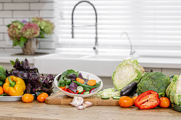 Frisches Gemüse bei der Zubereitung von Salat auf einem Holztisch vor dem Hintergrund einer modernen Küche Kopierraum. - Foto, Bild