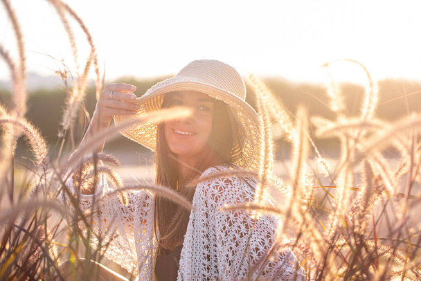 Porträt einer jungen Frau in der Sonne, die in Sommerkleidung und Hut auf einem Feld sitzt . - Foto, Bild