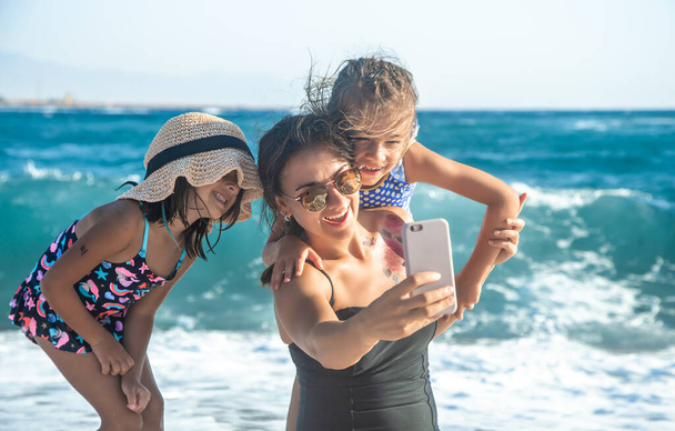 Eine Mutter mit Kind macht vor dem Hintergrund des Meeres und der Meereswellen ein Selfie. Das Konzept Familie und Erholung - Foto, Bild