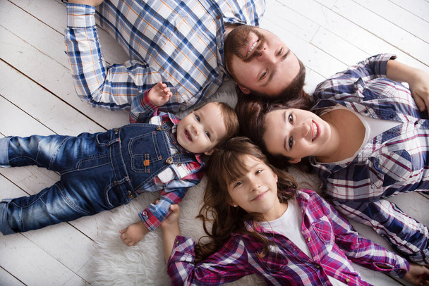 happy parents with daughter and son lying with plaid on floor at room, top view - Фото, изображение