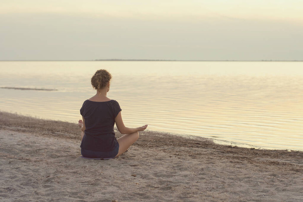 Una ragazza siede sulla riva del lago e medita - Foto, immagini