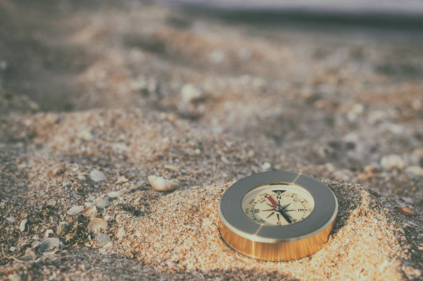 Μια πυξίδα που δείχνει την κατεύθυνση βρίσκεται στην άμμο με κοχύλια - Φωτογραφία, εικόνα
