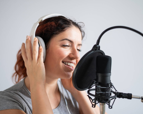 A woman with headphones is recording a song in a recording studio. Emotional girl sings with pleasure - Фото, зображення