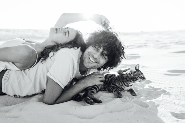 Cheerful young couple having fun on the beach with their bengal cat - Fotografie, Obrázek