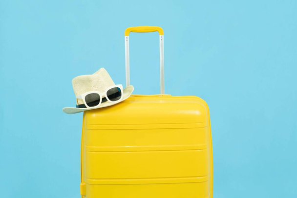 Summer time - Yellow suitcase or luggage with hat and sunglasses on pastel blue background minimal creative travel concept Holiday Adventure Trip. - Foto, imagen