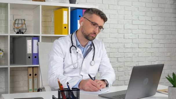 Médico en el hospital escribe síntomas en portátil escucha cliente utiliza la computadora - Foto, imagen