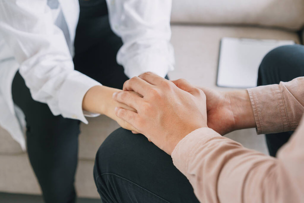 Close-up of psychiatrist hands together holding palm of her patient.  Psychological male comforting and holding a woman hand while sitting on the sofa. psychologist concept - Fotó, kép