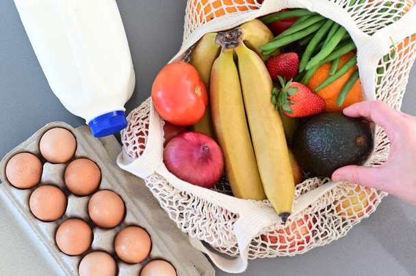 Nő kezét forgalomba egy bevásárló táska tele zöldségekkel és gyümölcsökkel otthoni konyha pulton. - Fotó, kép