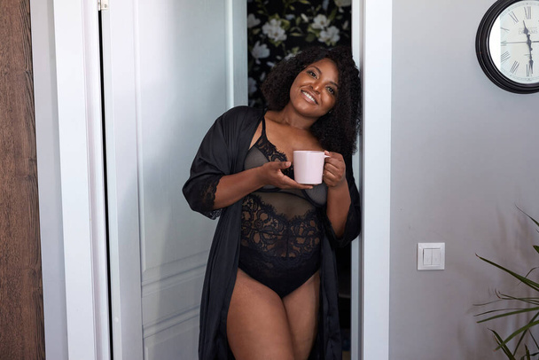 ελκυστική παχουλή μαύρη γυναίκα εισέρχονται δωμάτιο κρατώντας φλιτζάνι καφέ - Φωτογραφία, εικόνα