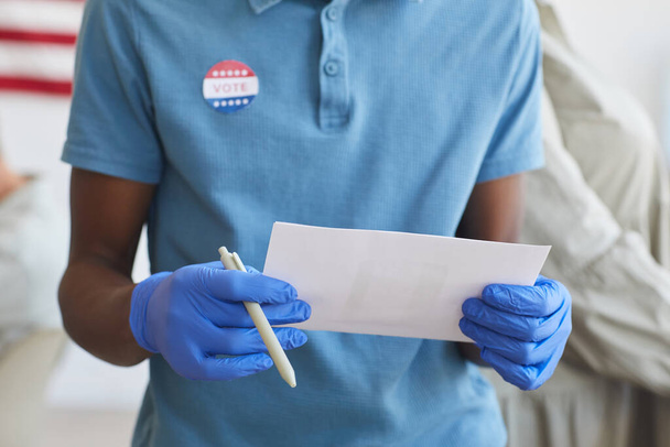 Cropped portrait of unrecognizable African-American man holding ballot and standing by voting booth on post-pandemic election day, copy space - Foto, afbeelding