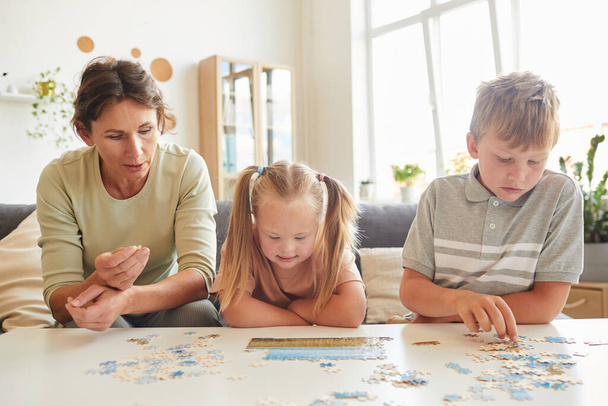 Fronte ritratto di famiglia amorevole con esigenze speciali bambino che gioca con puzzle e giochi da tavolo insieme a casa, copiare lo spazio - Foto, immagini