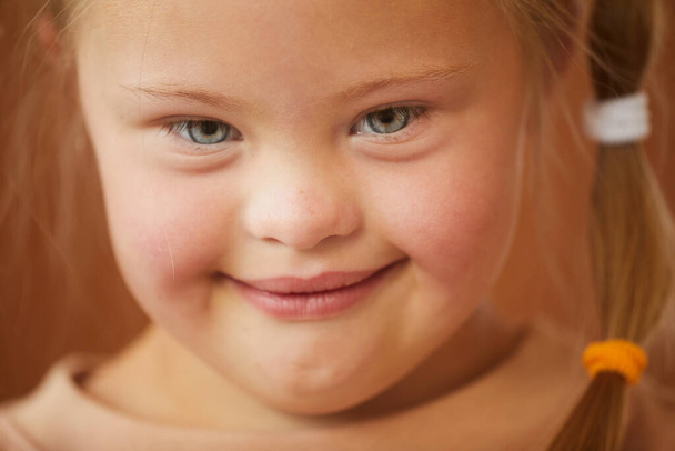 Nahaufnahme Porträt eines süßen Mädchens mit Down-Syndrom, das glücklich in die Kamera lächelt, Studioaufnahme - Foto, Bild