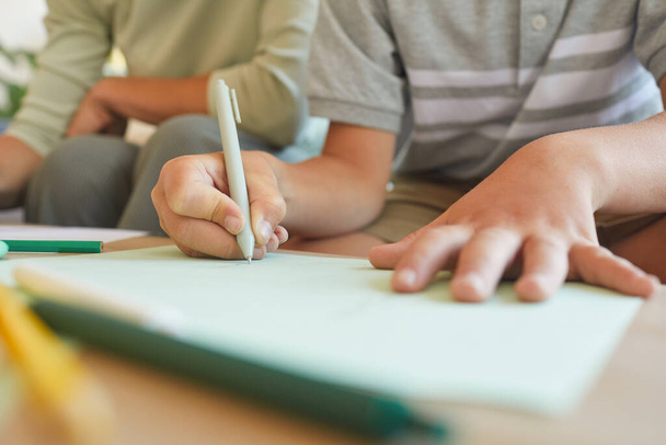 Close-up de escrita menino irreconhecível ou desenho durante a aula de desenvolvimento, foco na mão segurando caneta, espaço de cópia - Foto, Imagem