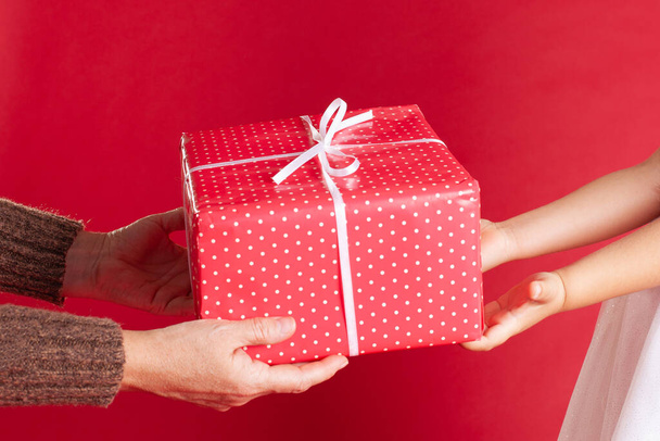 close up hands of parent and child holding a Christmas gift, buying and packing gifts for Christmas on a red background - Фото, изображение
