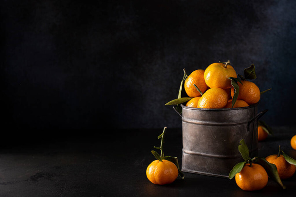 ripe small tangerines with leaves in an iron bowl on a dark background - Фото, зображення