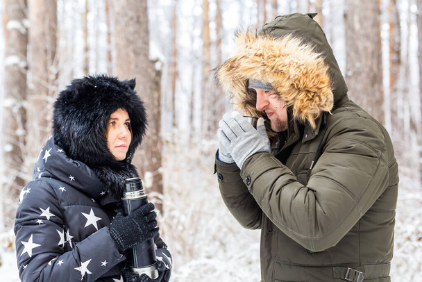 Season and walk concept - Happy couple drinking hot tea in winter forest - Fotografie, Obrázek