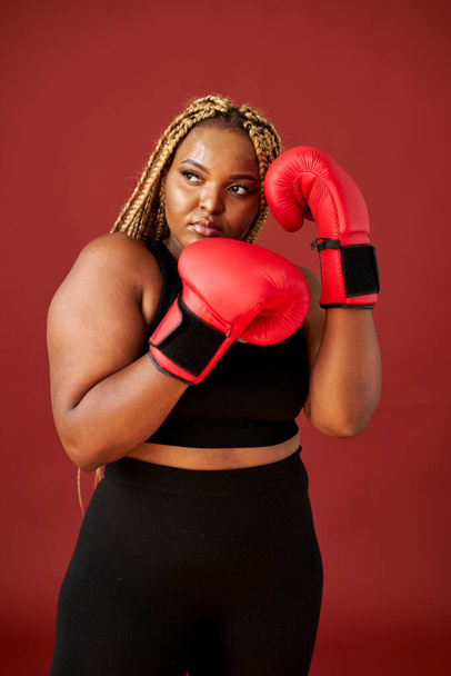 african oversize woman with red boxing mitts isolated on red background - Фото, изображение
