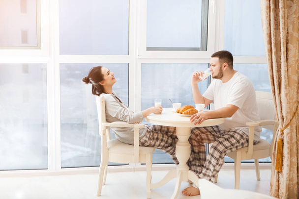 szczęśliwy młody para w miłość mając śniadanie w pobliżu okna w mieszkaniu  - Zdjęcie, obraz