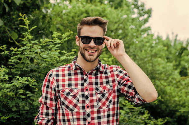 Perfect male. young unshaven man. sexy man wearing checkered clothes posing in park. Good confident young man standing and smiling in urban shirt. denim fashion style. handsome man with beard - Photo, image
