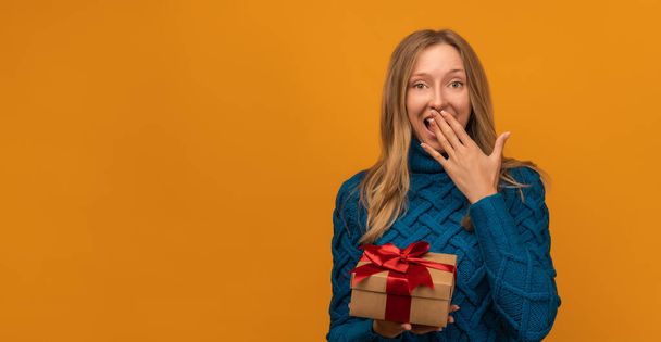Attraktive junge Frau mit Geschenk verziert mit Schleife posiert mit überraschtem Gesichtsausdruck auf gelbem Hintergrund. Neujahr, Frauentag, Geburtstag, Feiertagskonzept - Foto, Bild