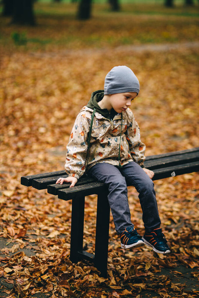 little child sitting on a bench in autumn park - Foto, Bild