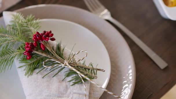 上のビューは、クリスマスの日にセットテーブルの上に折り畳まれたリネンナプキン装飾プレートに横たわっている松の小枝と果実のPANを閉じます - 映像、動画