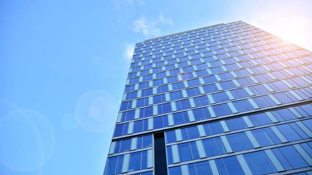 Blauwe gordijnwand gemaakt van gehard glas en stalen constructies onder blauwe hemel. Een fragment van een gebouw. Glazen gevels op een zonnige dag met zonnestralen aan de blauwe hemel. - Foto, afbeelding