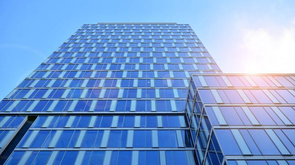 Mavi gökyüzünün altındaki tonlu cam ve çelik yapılardan yapılmış mavi perde duvarı. Binanın bir parçası. Parlak güneşli bir günde mavi gökyüzünde güneş ışınlarıyla cam cepheler.. - Fotoğraf, Görsel
