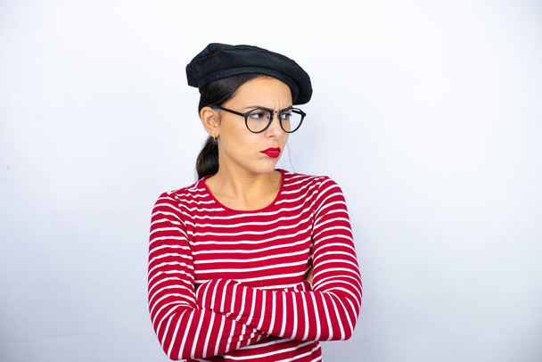 Giovane bella donna bruna indossa berretto francese e occhiali su sfondo bianco pensando cercando stanco e annoiato con le braccia incrociate - Foto, immagini