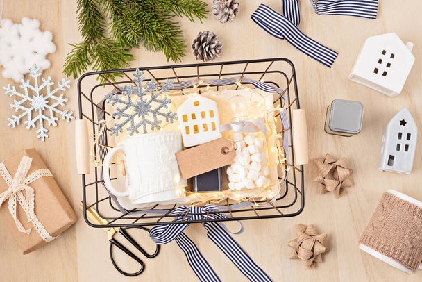 Preparing care package, seasonal gift box with marshmallow, tea,coffee or cacao box and christmas ornament. Personalized eco friendly basket for winter holidays. Top view, flat lay - Photo, Image