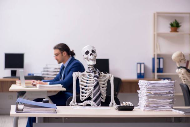Fiatal férfi alkalmazott csontvázakkal az irodában - Fotó, kép