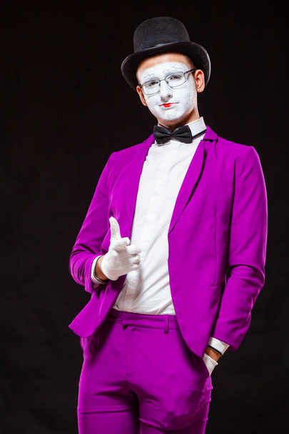 Portrait of male mime artist, isolated on black background. Man in purple suit points and smiles. Symbol of self confidence, victorious - Foto, imagen
