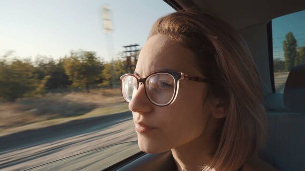 Dívka s brýlemi jezdí na zadním sedadle a dívá se z otevřeného okna. - Fotografie, Obrázek