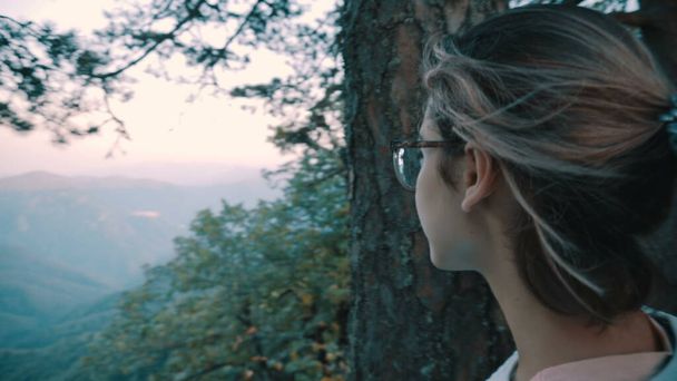 Una giovane ragazza con gli occhiali si trova sulla scogliera e guarda le montagne verdi. Vista dal retro. Viaggia tra le montagne. - Foto, immagini