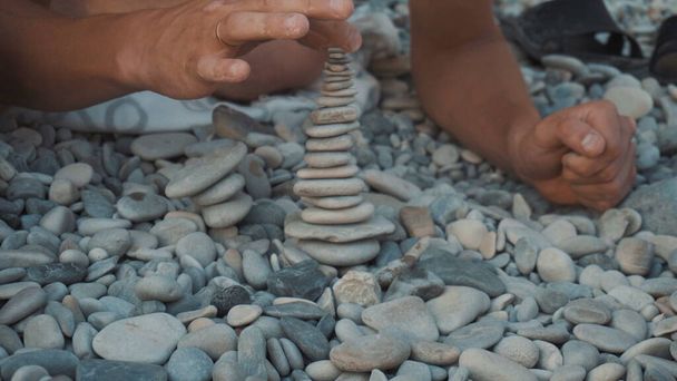 若い男がビーチに小石の塔を建て、それからそれは落ちる。タワーの閉鎖. - 写真・画像