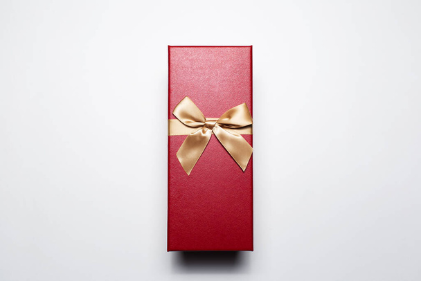 Κοντινό πλάνο του δώρου κουτί του κόκκινου χρώματος με χρυσό τόξο, απομονώνονται σε λευκό φόντο. - Φωτογραφία, εικόνα