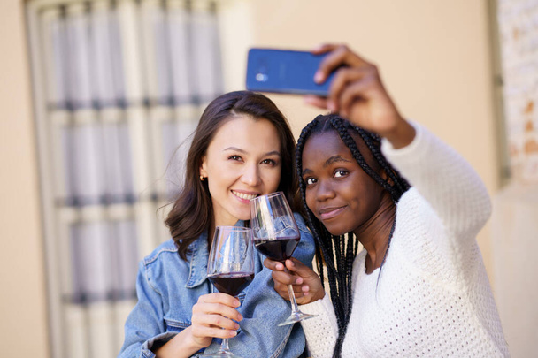 Deux femmes font un selfie avec un smartphone tout en prenant un verre de vin. - Photo, image