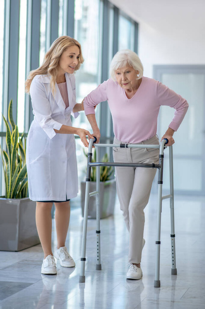 Female doctor in a lab coat walking with a senior patient with rolling-walker - Foto, imagen