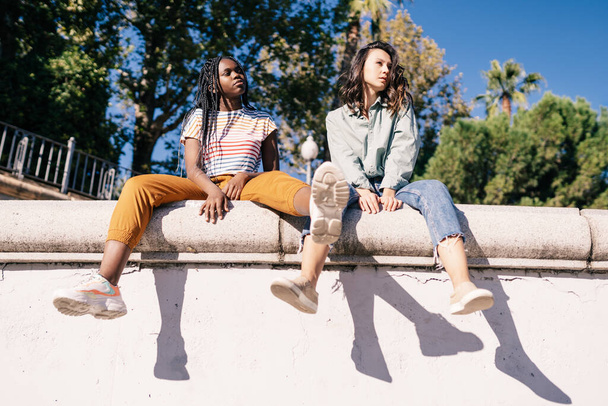Deux femmes multiethniques assises sur un mur urbain. - Photo, image