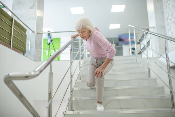 Senior woman in pink shirt falling down on the stairs - 写真・画像
