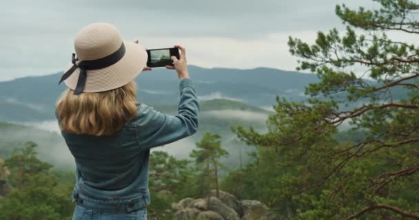 Nainen seisoo jyrkänteellä. Hän ottaa kuvia kauniista vuoristomaisemasta. 4K DCI - Materiaali, video