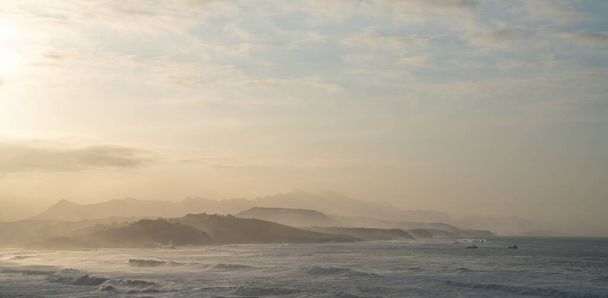 Дикое побережье океана на закате с волнами разрывающимися и горами в силуэте позади - Фото, изображение