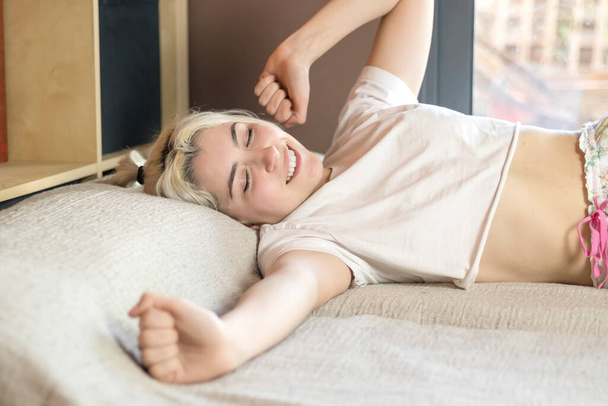Portrait of attractive lovely girl enjoying time in bad after sleeping lying on bed making stretching keeping eyes closed. Good day life health concept - Фото, изображение