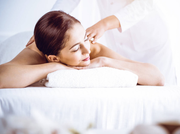 Beautiful brunette woman enjoying back massage in sunny spa center. Beauty and medicine concept - Foto, imagen