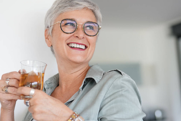 Cheerful 50-year woman drinking hot tea at home - Foto, afbeelding