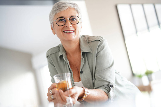 Vrolijke 50-jarige vrouw die thuis warme thee drinkt - Foto, afbeelding
