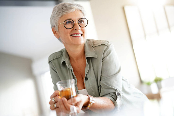 Cheerful 50-year woman drinking hot tea at home - Foto, Imagen