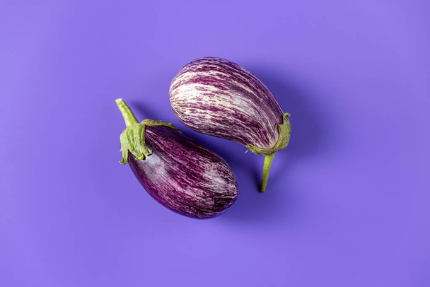 Deux aubergines fraîches crues différentes sur fond violet. Concept de style de vie maison verte et produits de l'agriculture de subsistance, pose plate, espace de copie - Photo, image