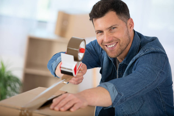 man moving in a new apartment packing and taping boxes - Foto, imagen