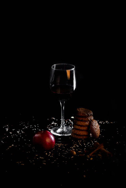 A glass with wine, apple and cookies on black background - Photo, image